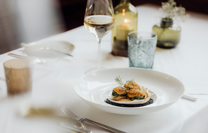 Elegant angerichtete, gratinierte Jakobsmuschel begleitet von einem exklusiven Weißwein im Restaurant der Stasta.