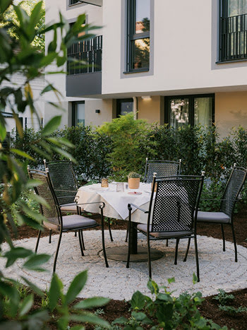 Umrahmt von Pflanzen befindet sich ein elegantes Sitzensemble im Gastgarten des Stasta.